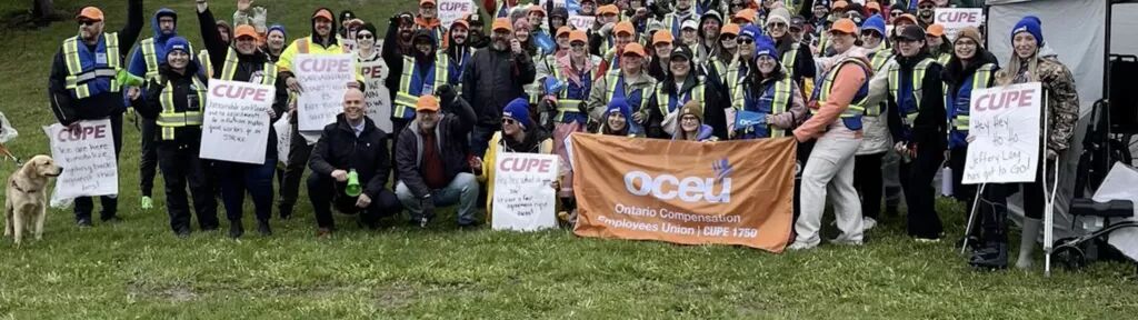 OCEU workers on strike at WSIB pose for a photo outside a picket with a large OCEU banner