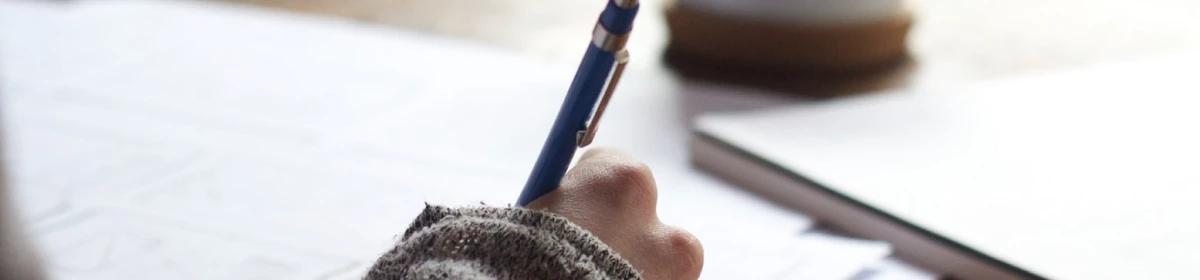 Image of hand holding a pen and writing on paper