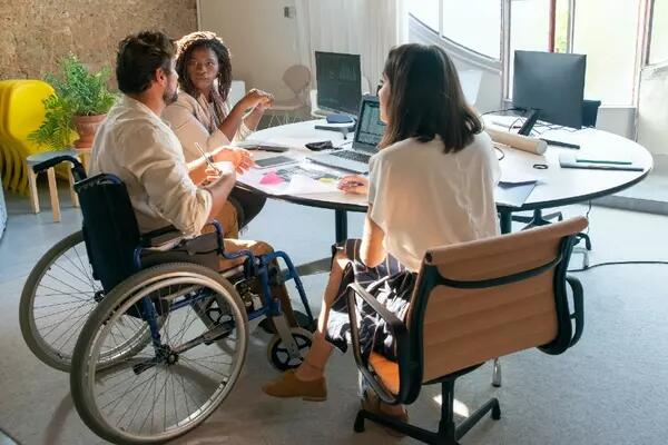 Group of people, one of whom is using a wheelchair, gathered around a conference table in an office