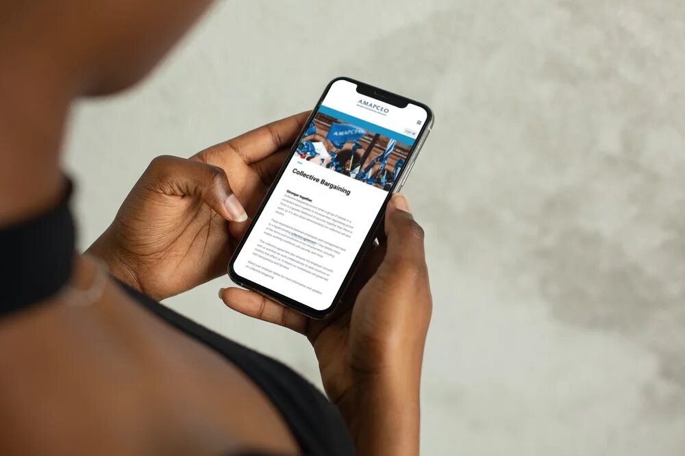 A member holding a smartphone displaying the AMAPCEO Collective Bargaining webpage