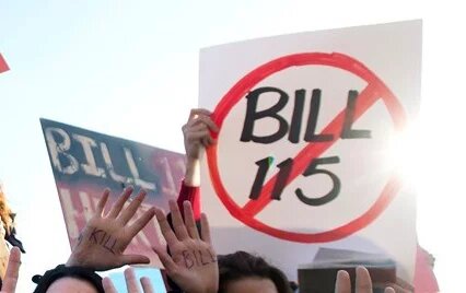 A sign with "Bill 115" in the centre of a red circle with a line through it