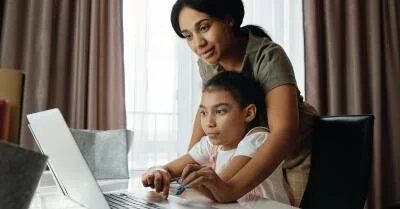 An image of a mother helping her daughter use a laptop