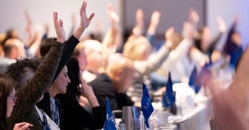 members raising hands at a conference