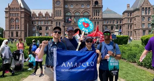 Activists holding an AMAPCEO flag and paid sick days sign in front of Queen's Park