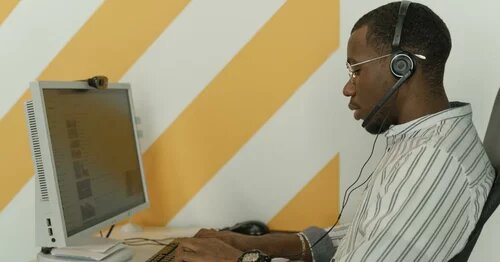 A person in an office typing on a laptop wearing a headset