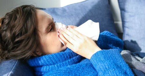 A person lying on a couch blowing their nose