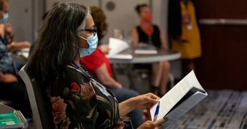 A masked member reading the agenda at AMAPCEO's WPR conference in 2022