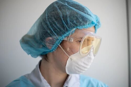 A person in a respirator mask, scrubs, a hairnet, and goggles