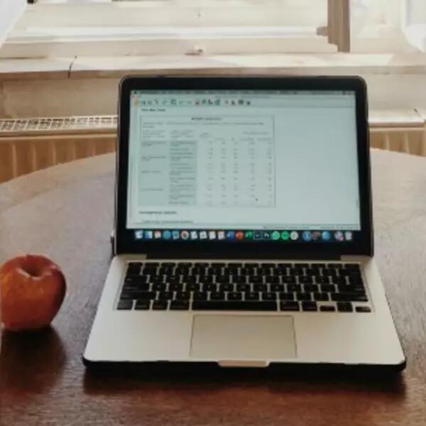 A laptop on a kitchen table with a glass of water and an apple next to it