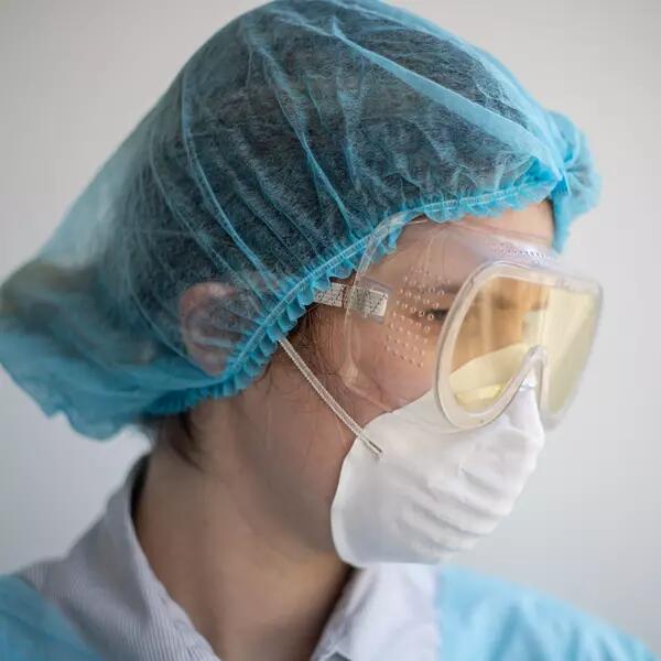 A person in a respirator mask, scrubs, a hairnet, and goggles